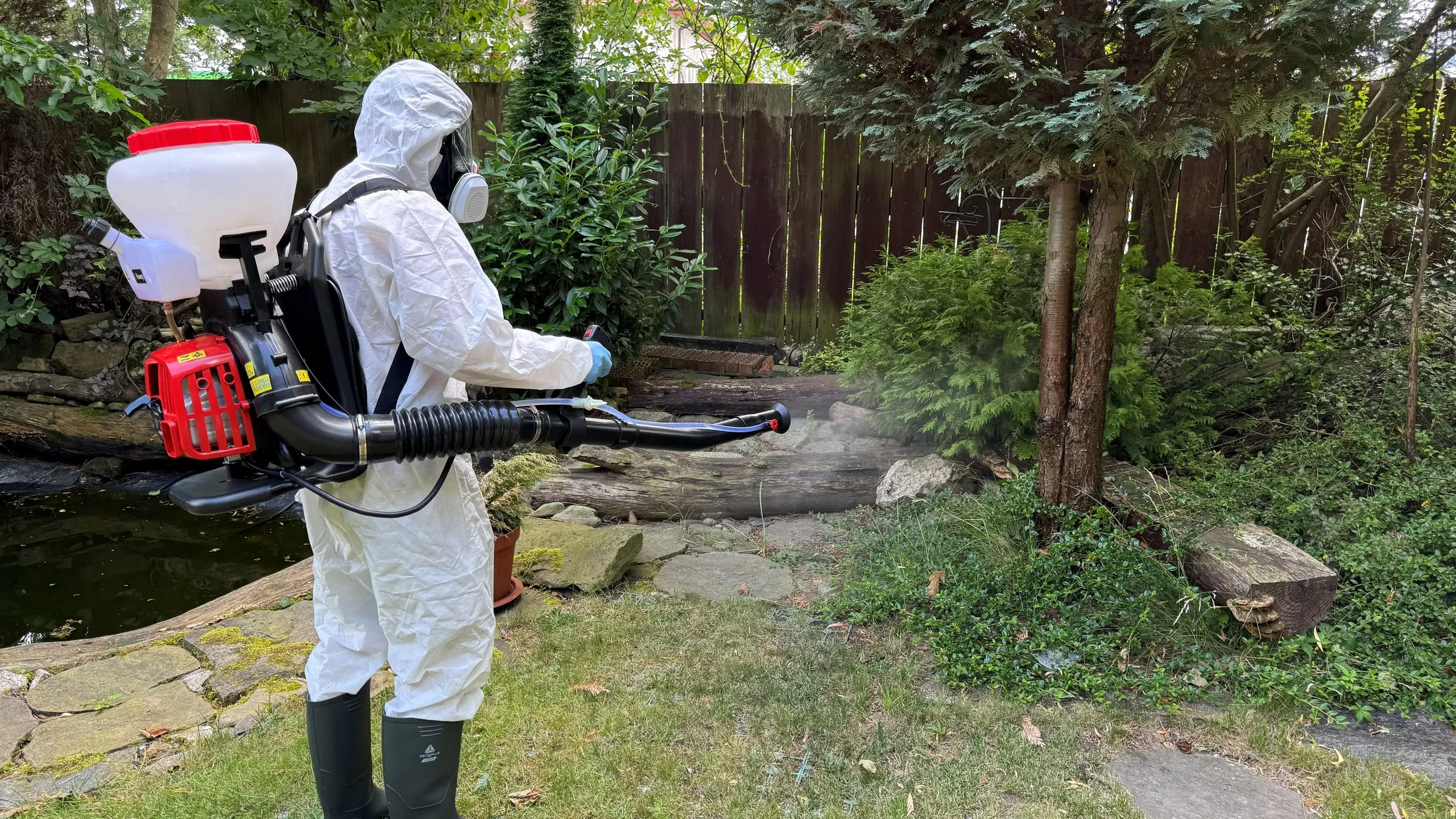Technik Venator Pestis wykonuje oprysk ogrodu na kleszcze i komary opryskiwaczem plecakowym